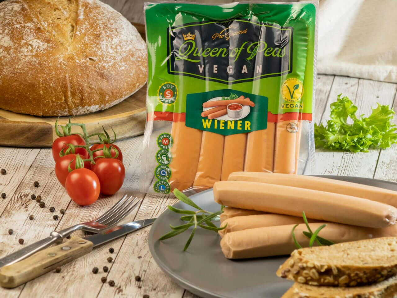 Vegan Wiener Sausages package with fresh bread, tomatoes, and herbs on a wooden table, highlighting a plant-based, healthy, meat-free option.