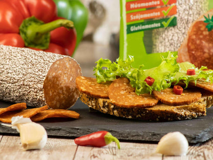 Vegan piquant pea salami slices on oat bread with fresh lettuce, surrounded by bell peppers, garlic, and chili peppers.