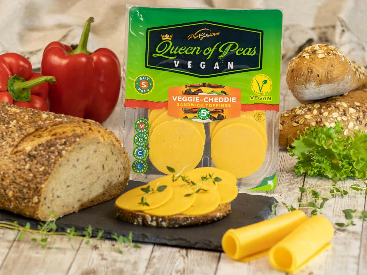 Veggie-Cheddie vegan sandwich toppings by Queen of Peas placed near fresh bread, bell pepper, and lettuce.